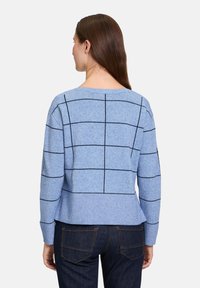 Blau gestrickter Pullover mit einem lässigen Schnitt, der schwarze Karos aufweist. Der Stoff hat eine weiche Textur und einen gerippten Saum. Wird mit dunklen Jeans kombiniert.