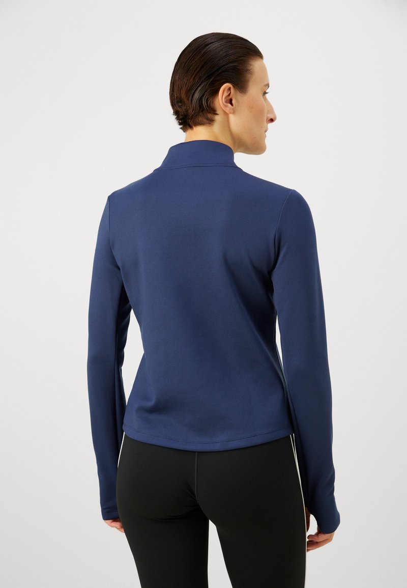 Marine langærmet polo i en glat stof, med en spidse krave og et tætsiddende design, parret med sorte leggings.