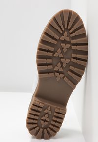 Semelle en caoutchouc marron avec motif de bande de roulement, taille 37, fixée à une tige blanche. Caractérisée par une finition texturée et un design d'orteil arrondi.