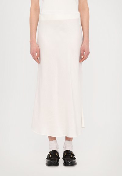 Jupe midi blanche en tissu lisse avec une fente sur le côté et une coupe décontractée. Associée à des chaussures noires et des chaussettes blanches à la cheville.