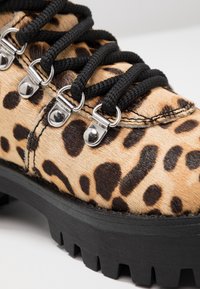 Bottines à imprimé léopard avec un dessus en fourrure texturée, des lacets noirs, des œillets métalliques, et une semelle épaisse en caoutchouc noir avec un bord dentelé.