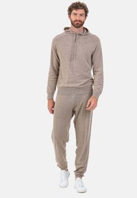 Ensemble de vêtements d'intérieur en maille marron clair comprenant un haut à capuche avec cordons de serrage et un pantalon assorti, tous deux dotés de poignets côtelés et de poches.