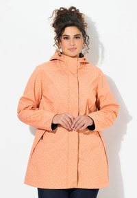 Chaqueta impermeable naranja con capucha, que presenta un patrón de puntos, mangas largas y bolsillos laterales, hecha de material ligero.