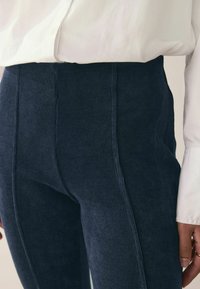 Tengerészkék bordás leggings magas derékkal, texturált anyaggal és oldalsó varrásokkal, fehér gombos inggel párosítva.