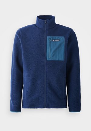 Marineblauwe fleecejas met een hoge kraag, voorzien van een contrasterende blauwe ritszak op de borst en twee zijzakken. Zachte, gestructureerde stof.