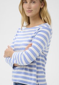 Bluza cu mânecă lungă în dungi albastre și albe, cu gât rotund, textură moale, croială lejeră și despicături laterale.