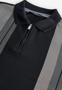 Polo noir et gris à rayures avec une texture côtelée, doté d'une fermeture à glissière au milieu et d'un col contrastant.