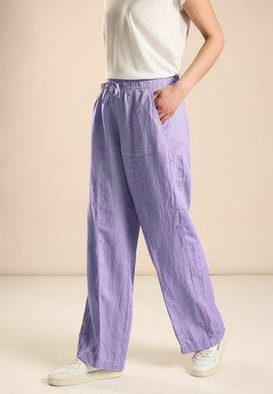 Pantaloni in lino viola chiaro con una vestibilità rilassata, vita con elastico e cordino, tasche laterali e texture liscia, abbinati a sneakers bianche.
