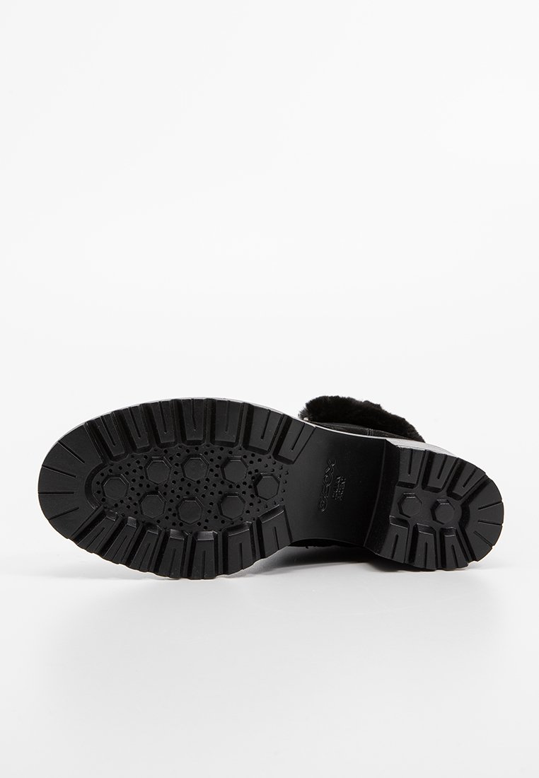 Calzado negro con suela de goma texturizada, que presenta una puntera redondeada y una parte superior suave similar al pelo. La suela muestra un patrón de panal para mayor agarre.