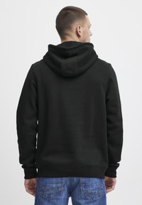 Black cotton hoodie with a spacious hood, ribbed cuffs, and waistband. Worn with blue denim jeans, showing a casual back view.