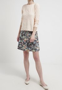 Světlé růžové texturované tričko s dlouhým rukávem v kombinaci se sukní se šedivým květinovým vzorem. Outfit doplňují béžové baleríny.