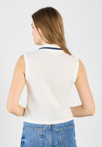 Hvit polo skjorte uten ermer med marineblå krage og en tettsittende design, laget av myk stoff med en litt teksturert overflate.