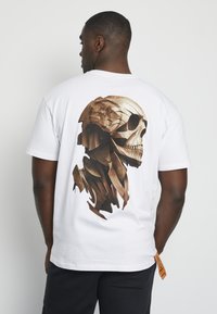 White t-shirt featuring a large, detailed brown wooden skull graphic on the back. Short sleeves and a rectangular shape.