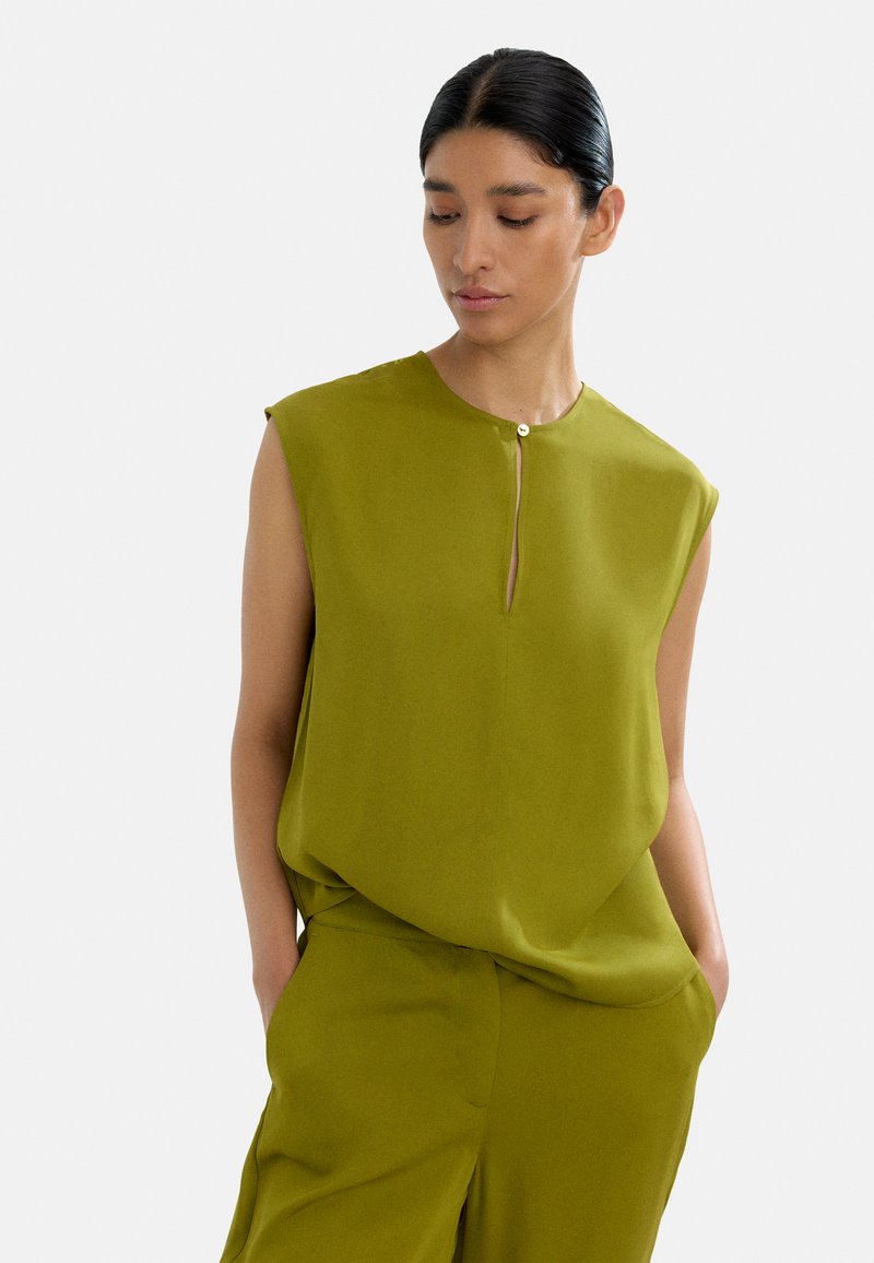 Bezramionowa oliwkowozielona bluzka z okrągłym dekoltem, z dziurką w kształcie klucza i małym guzikiem z przodu. Gładka struktura materiału.