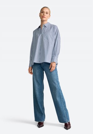 Striped button-up shirt in blue and white, paired with high-waisted, wide-leg blue jeans. Includes pointed toe shoes, presenting a relaxed fit.