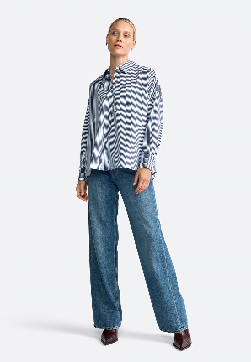 Gestreifte Button-Down-Bluse in Blau und Weiß, kombiniert mit hoch taillierten, weit geschnittenen blauen Jeans. Mit spitzen Schuhen, die eine entspannte Passform bieten.