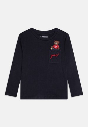 Marineblauw shirt met lange mouwen en een klein zakje met een teddybeer die een rood shirt draagt en de rode tekst "guess" op het zakje geborduurd.