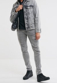 Veste en denim gris avec des détails déchirés, associée à un jean gris déchiré et des baskets montantes noires. Sac à bandoulière noir simple en accent.