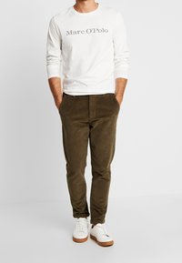 Witte blouse met lange mouwen met "Marc O'Polo" branding, gecombineerd met olijfgroene corduroy broek en witte sneakers met bruine zolen.