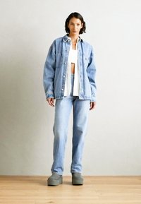 Př oversized modrá džínová bunda, bílý kratší top, světle modré džíny a šedé platformové boty. Jednoduchý design s minimálními detaily.