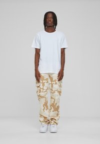 White short-sleeve t-shirt, beige and cream camouflage cargo pants with large pockets, and white sneakers on a neutral background.