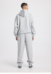 Grijze sweatstof trui en bijpassende broek gemaakt van zachte stof. De hoodie heeft een grote capuchon, terwijl de broek elastische boorden en een ontspannen pasvorm heeft.