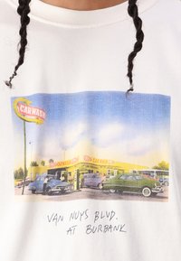 Hvid t-shirt med en vintage bilvask-illustration i gul og blå, med retrobiler og håndskrevet tekst nedenfor.