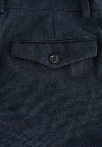 Nahaufnahme eines dunkelblauen strukturierten Stoffs mit einer Tasche, die einen schwarzen Knopf und subtile Nähdetails aufweist.