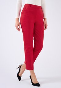 Pantalones ajustados rojos con textura suave, corte slim y cierre de botones, combinados con tacones negros puntiagudos.