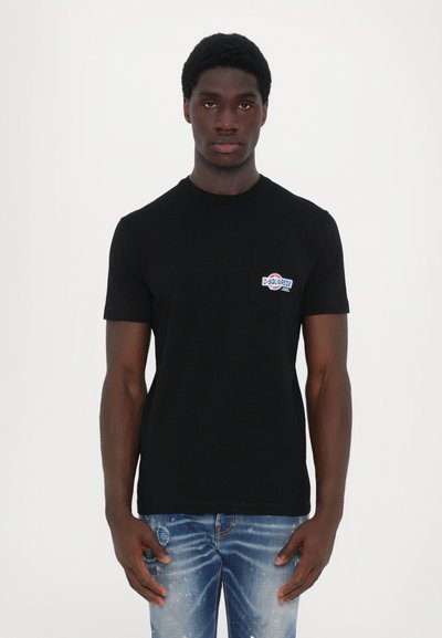 T-shirt en coton noir à manches courtes, avec un petit badge logo multicolore sur la poche poitrine gauche, associé à un jean en denim clair.