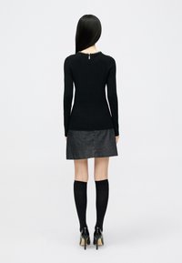 Μαύρο πλεκτό τοπ με μακριά μανίκια, ριμπ υφή και κλείσιμο στην πλάτη με άνοιγμα σε σχήμα δακρύου. Συνδυασμένο με σκουρόχρωμη γκρι τζιν φούστα και μαύρες καλτσοφόρες μέχρι το γόνατο.