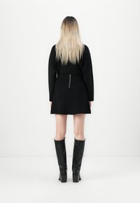 Abito lungo nero a maniche lunghe con vita aderente e dettaglio con zip sul retro, abbinato a stivali neri in pelle al ginocchio.