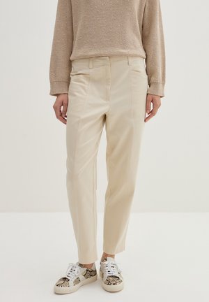 Beige højttaljede bukser kombineret med en beige striktrøje og hvide sneakers med slangeprintdetalje.