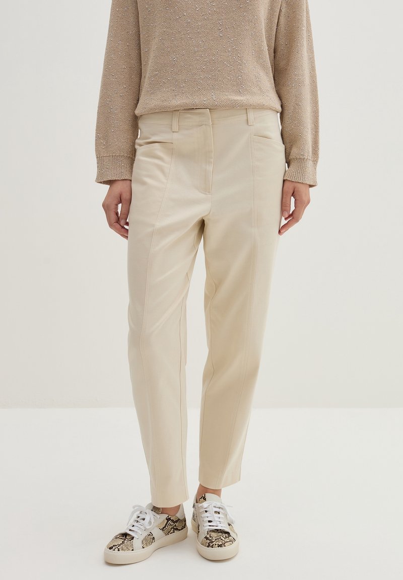 Pantalon beige taille haute associé à un pull en maille beige et des baskets blanches avec un détail imprimé serpent.