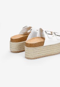 Sandali platform bianchi con due fibbie argento, una morbida soletta in sughero e un tacco in juta intrecciata. Parte superiore bianca texturizzata e suola di colore naturale.