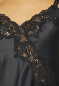 Svart satin cami med intrikate svarte blonder langs halsen, justerbare stropper og glatt tekstur.
