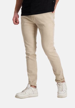 Beige katoenen broek met een slim fit, voorzien van een klassieke vijf-pocketontwerp, gecombineerd met witte sneakers. Soepele textuur en strakke lijnen.