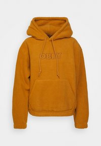 Orange fleece-jacka med huood och stor framficka samt dragsko. Har "OBEY" tryckt i en kontrasterande brun färg.