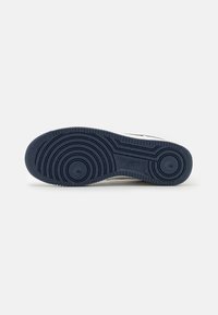 Semelle de chaussure en caoutchouc noir avec des motifs circulaires d'adhérence et le logo Nike au centre sur fond blanc.