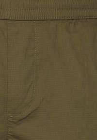 Tissu vert olive avec une texture lisse, présentant des lignes verticales côtelées et une poche en couture près de la taille.