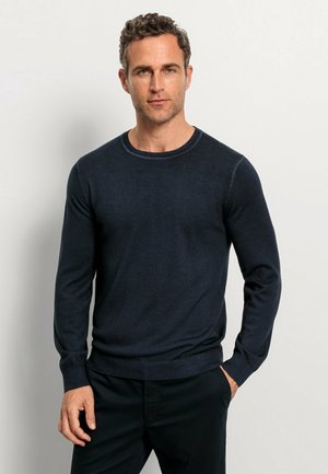 Dunkelblauer Rundhalsausschnitt-Pullover aus weichem Strickstoff, mit langen Ärmeln und gerippten Bündchen, getragen über dunklen Hosen.