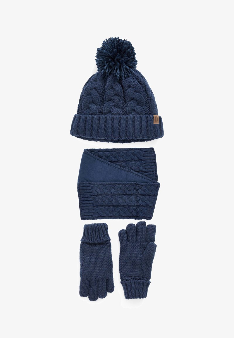 Tengerész kék kötött sapka pom-pom-mal, hozzá illő sál, amely fonott kötésmintával rendelkezik, és ujjatlan kesztyűk. Minden darab texturált kötött mintát mutat be.