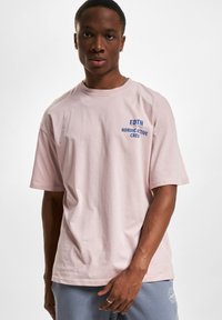 Lyserød bomulds t-shirt med korte ærmer, rund hals og blå tryk med teksten "EDTN NORDIC ACTIVE CREW" på brystet. Enkel design.