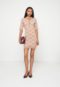 Vestido bege de manga curta com padrão de logo, gola e comprimento até a coxa. Combinado com uma bolsa bordô e sapatos de salto agulha.