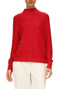 Roter Strickrollkragenpullover mit langen Ärmeln und gerippten Bündchen. Weiche Textur und lockere Passform, kombiniert mit hellen Hosen.