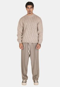 Maglione beige lavorato a maglia con motivo texturizzato, abbinato a pantaloni grigi chiari plissettati e sneaker bianche e nere.