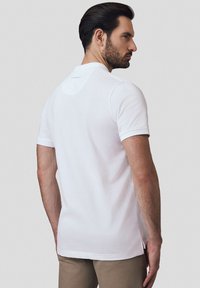 Biała koszulka polo wykonana z bawełny, charakteryzująca się dopasowanym krojem, krótkimi rękawami i subtelnym logo na karku. Doły z bocznymi rozporkami.