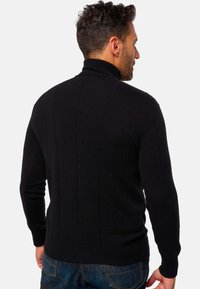 Schwarzer gestrickter Pullover mit hohem Kragen, vertikalen Nähten und langen Ärmeln, kombiniert mit blauen Denim-Jeans. Rückansicht.