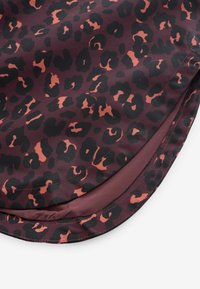 Kokkupandud kangas tumepunakaspruuni põhjaga ning musta ja põlenud oranži leopardimustriga, kus on nähtav osa paelast ja sisevoodrist.