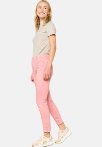 Maglietta grigia chiara a maniche corte abbinata a jeans rosa aderenti con dettaglio zip alla caviglia. Il modello indossa sneakers beige.